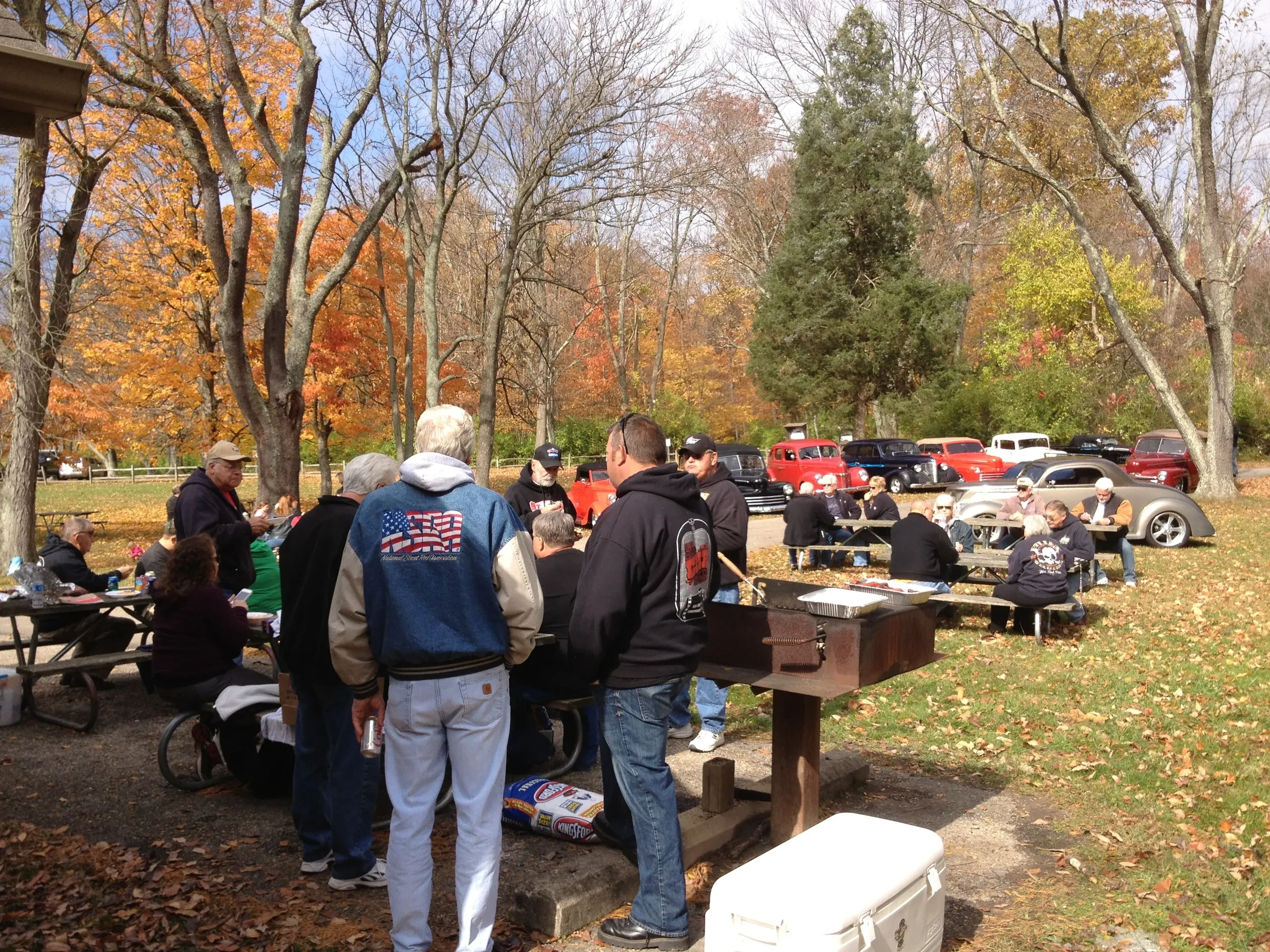Members gathered at autumn park picnic with vintage cars